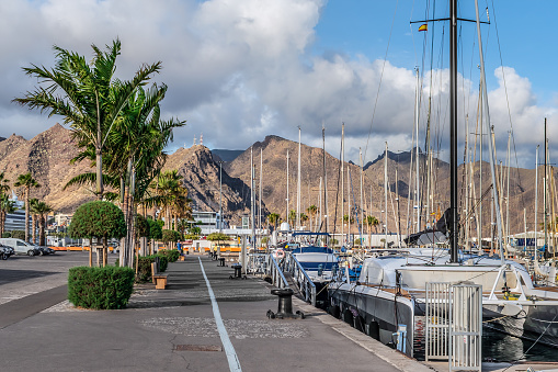 Santa Cruz de Tenerife, Spain - November 24, 2021: Promenade in the port of Santa Cruz de Tenerife. Many yachts are moored off the coast of the Atlantic Ocean against the backdrop of the mountains