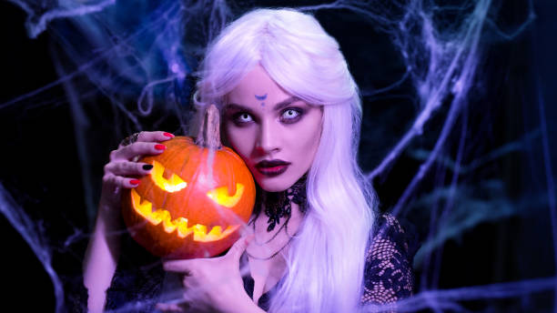 Sexy witch with hallowen makeup and long white hair holding pumpkin on black background stock photo