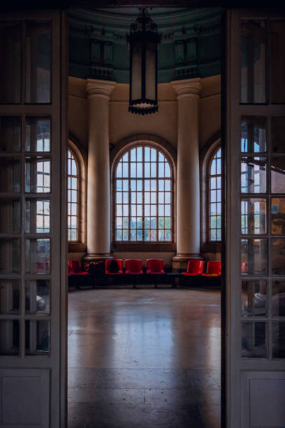Coimbra, Portugal - September 21, 2022: Detail of empty waiting room at Coimbra train station with red plastic chairs and the morning light coming through the big windows seen from the open entrance door