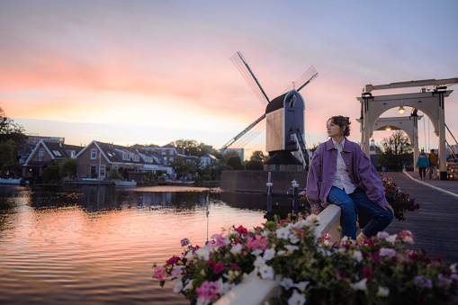 Young Caucasian woman in purple coat standing near the windmill in Leiden at sunset