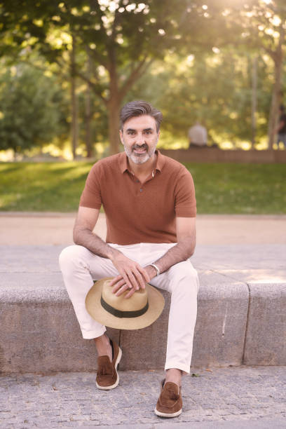 istock Relaxed middle-aged man looking at camera while sitting on a bench in a park. 1425978615