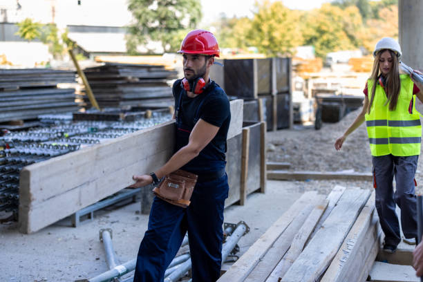 istock Young Construction Worker is Carrying a Wooden Plank at a Construction Site. 1425980801