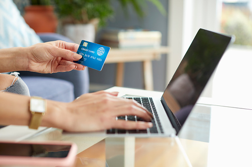 Hands of female holding credit card and typing on laptop. Young woman is doing online shopping at home. She is doing payment through internet.