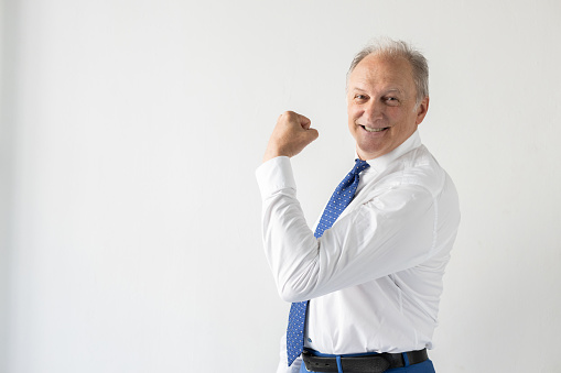 Portrait of successful mature businessman showing muscle. Senior manager wearing shirt and tie looking at camera and smiling, posing against white background. Success and leadership concept