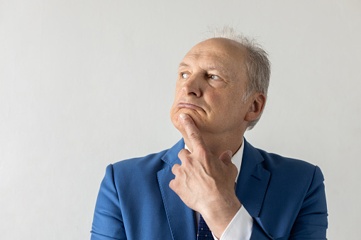 Close-up of pensive face of mature businessman. Senior manager wearing formalwear standing with hand on chin and looking away against white background. Business plans and aspirations concept