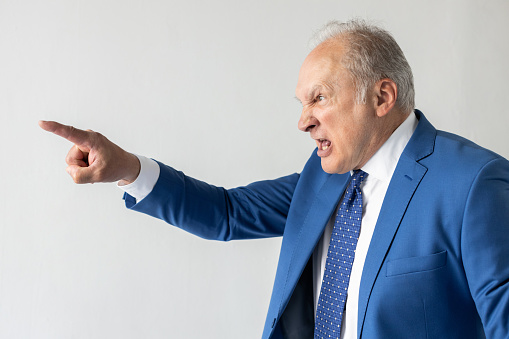 Portrait of angry mature businessman pointing at someone. Senior manager wearing formalwear looking away and blaming someone against white background. Angry boss concept