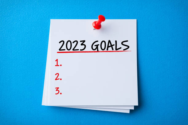 White Sticky Note With New Year 2023 Goals And Red Push Pin On Blue Cardboard Background stock photo