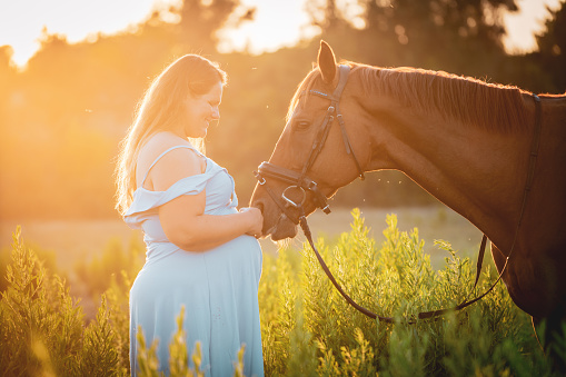 Portrait of pregnant mid adult woman enjoying with her horse and her baby in nature.