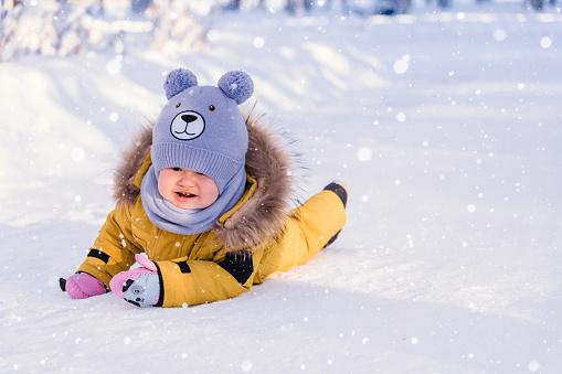 Toddler 12-17 months old in yellow winter clothes slipped and cries while walking in a winter park