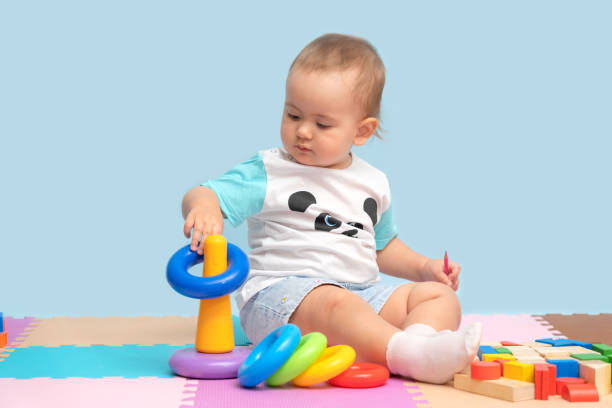 the kid collects the pyramid toy by putting colorful rings on the plastic tower base while sitting on the soft floor in the playroom. - criança de 1 a 2 anos imagens e fotografias de stock