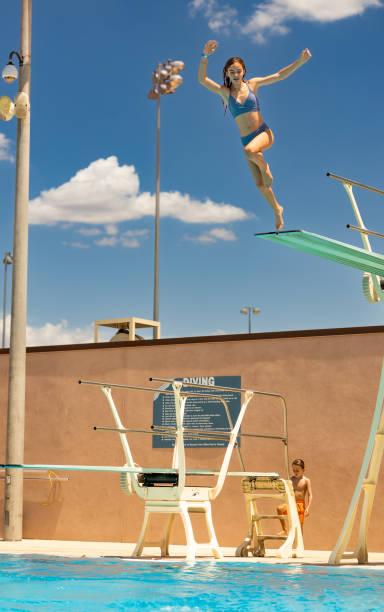 adolescente pula de prancha de mergulho acima da piscina - floodlight blue sky day - fotografias e filmes do acervo