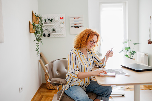 Portrait of a young adult woman checking her energy bills at home, sitting in her home office. She has a worried expression