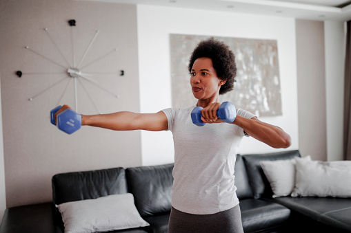 Determined woman losing weight at home and exercising with dumbbells. Sporty pretty woman exercising at home with dumbbells. Fitness, workout, healthy living and diet concept.