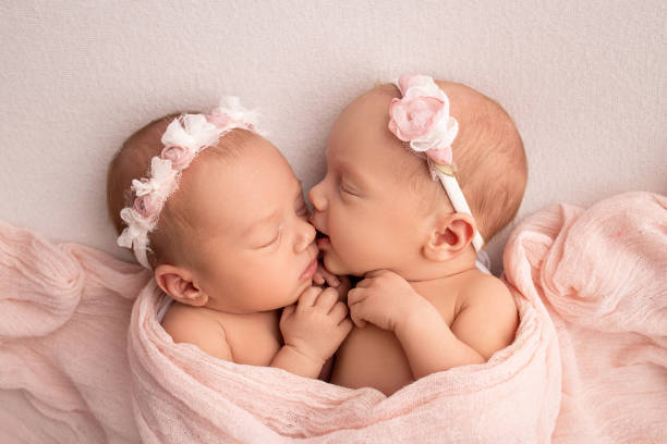piccole gemelle appena nate. un gemello appena nato dorme accanto a sua sorella. ragazze gemelle appena nate sullo sfondo di una coperta rosa con bende rosa. le ragazze abbracciano e baciano delicatamente la sorella in una posa carina. - twin newborn baby baby girls foto e immagini stock