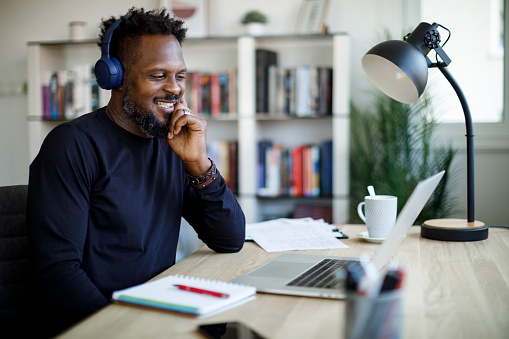 Smiling man with wireless headphones following online courses on his laptop at home