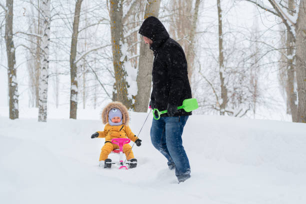 istock A happy father pulls a children's snowcat through the snow with a joyful child sitting on it in yellow warm clothes 1426014992