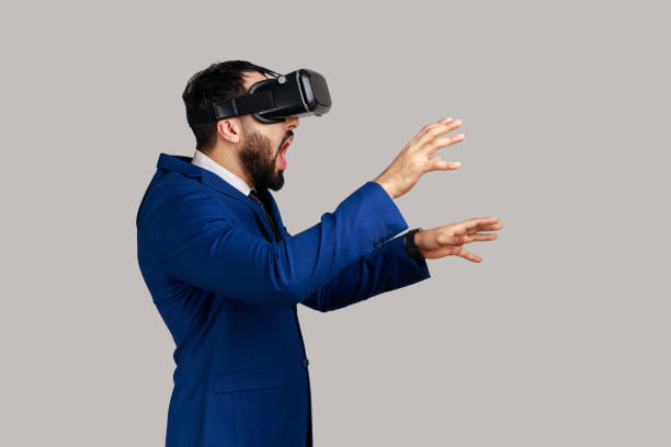 Side view of man playing virtual reality game with shocked facial expression, outstretching hands.