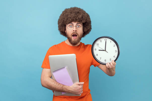 istock Man holding paper notebook and laptop, showing big wall clock, deadline. 1426026711