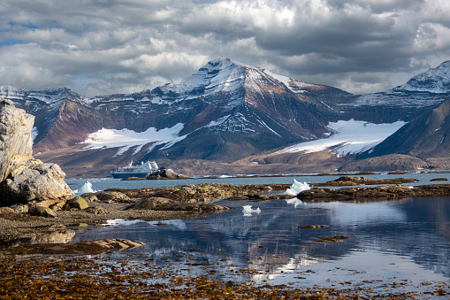 rugged landscape and fjords in rugged landscape and fjords in Svalbard with an expedition ship in the background