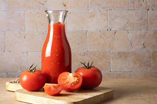 Glass bottle with homemade tomato sauce and ripe whole and chopped tomatoes on the table. Selective focus. Place for text.