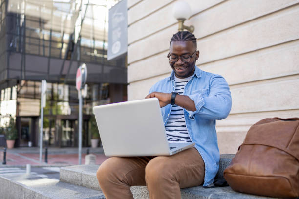 istock Smiling handsome man using laptop and checking time on wristwatch 1426028089