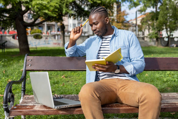 istock Serious male student holding a book and reading from laptop 1426028212