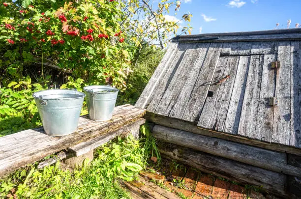 Metal buckets with water on a bench near a village well on a sunny day at the countryside
