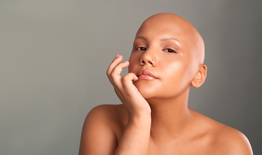 Face portrait of bald woman with cancer, alopecia or hair loss standing against grey studio background mockup. Strength, motivation or feminism empowerment of queer, LGBTQ or trans young beauty girl