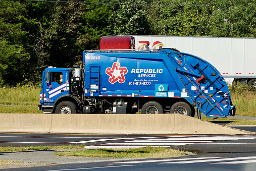 Fairfax, Virginia, USA - September 21, 2022: A Republic Services garbage truck travels through an intersection as a tractor-trailer turns behind it.