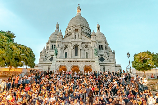 The Basilica of Sacred Heart in Montmartre or Sacré Coeur or Sacré-Cœur. Low angle view crown of people sitting in the stairs at the golden hour with a clear blue sky