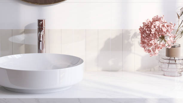 Modern and luxury bathroom vanity counter top with white round ceramic washbasin in sunlight from window with vase of pink flower