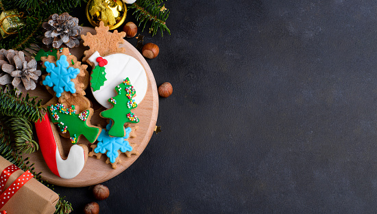 Christmas cookies background. Christmas gingerbread cookies with sugar paste and natural fir tree and Christmas decoration on dark background. Christmas banner, top view, flat lay, copy space