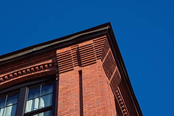 Decorative red brick cornice on 19th century textile mill building set against bright blue sky. The Davis and Furber Machine Co mill in the Machine Shop Village Historic District of North Andover