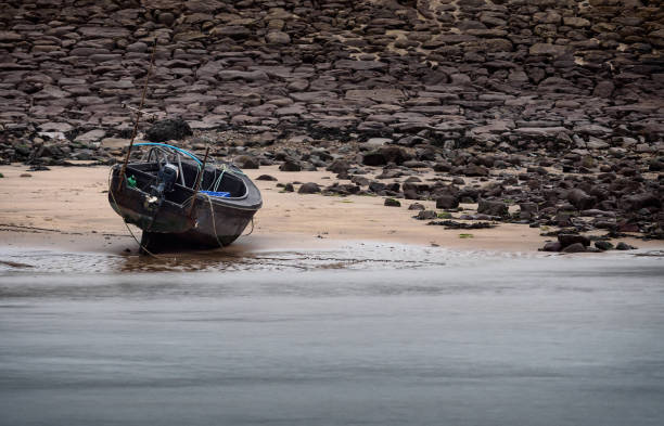 A beached boat, high on the sands, waits for the tide to return. A calm sea laps against the shore.