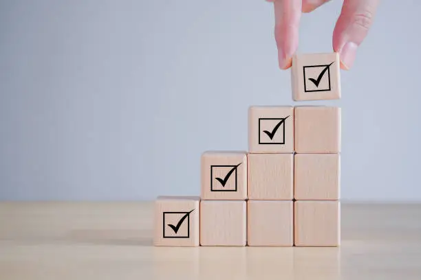 Photo of Checklist, Task list, Survey and assessment, Quality Control, Goals achievement and business success. Elections and Voting, Vote, to do list, Hand holding Check mark on ladder stack wooden blocks.