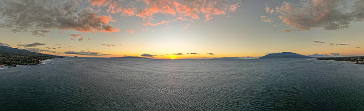 A panorama photo that features a falling sunset over the ocean off the shores of Oahu, Hawaii.