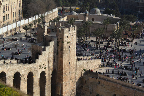 Aleppo, Syria - March 18, 2011: Before the war. People in front of the impressive medieval Citadel of Aleppo, a fortified castle in the center of the old city, a UNESCO World Heritage Site, and one of the oldest and largest castles in the world.
