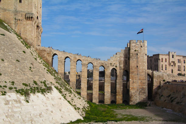 Aleppo, Syria - March 18, 2011: Before the war. People in front of the impressive medieval Citadel of Aleppo, a fortified castle in the center of the old city, a UNESCO World Heritage Site, and one of the oldest and largest castles in the world.