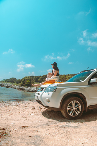 happy woman at sea summer beach sitting at car hood vacation concept