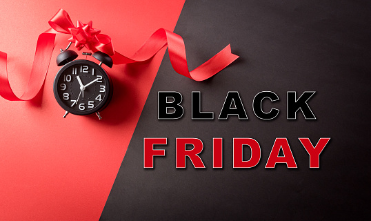 Top view of Black Friday decoration made from alarm clock,  ribbon on red and black background. Shopping concept boxing day and Black Friday composition.
