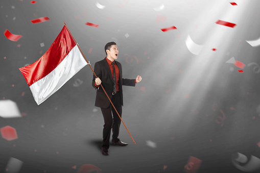 Asian businessman holding an Indonesian flag with a confetti background. Indonesian independence day