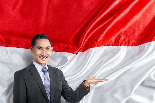 Asian businessman with open palm showing something with a red and white flag background. Indonesian independence day