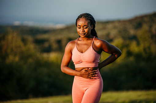 Cropped image of a beautiful African American woman, enjoying her breathing and chi practice outdoors, in nature, smiling, and focused on breathing. She's wearing a peach sports outfit