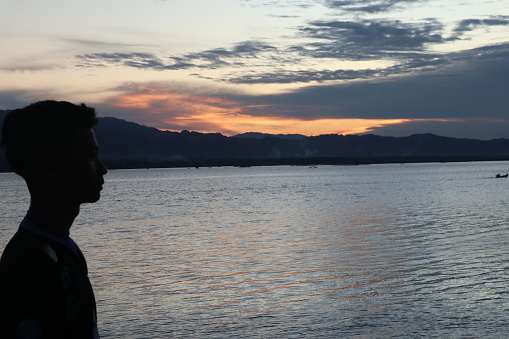 Silhouette of a young man standing by the lake enjoying the sunset. peaceful atmosphere in nature