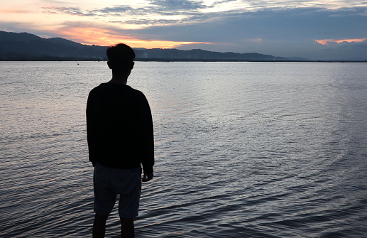 Silhouette of a young man standing by the lake enjoying the sunset. peaceful atmosphere in nature