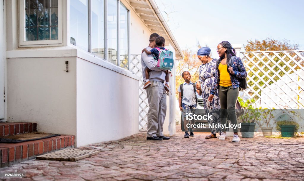 Parents greeting their three smiling children after school Smiling African parents meeting their three children outside their home after arriving back from school Building Exterior Stock Photo