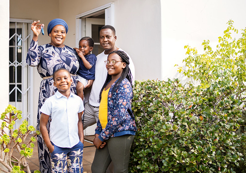 Portrait of a smiling African family standing with keys at the front of their new home