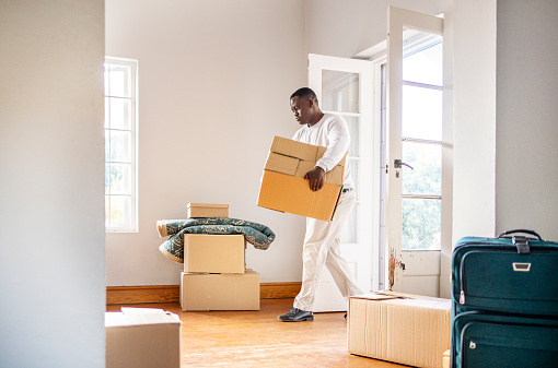 African man walking through a door into a living room carrying a box while moving house