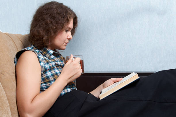 istock Woman with curly hair reading a book on sofa 1426131137