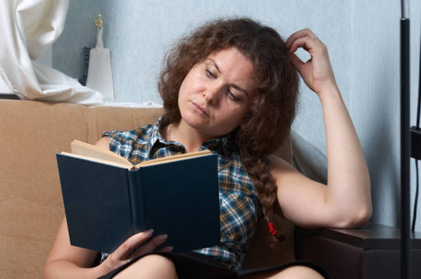 istock Woman with curly hair reading a book on sofa 1426131533